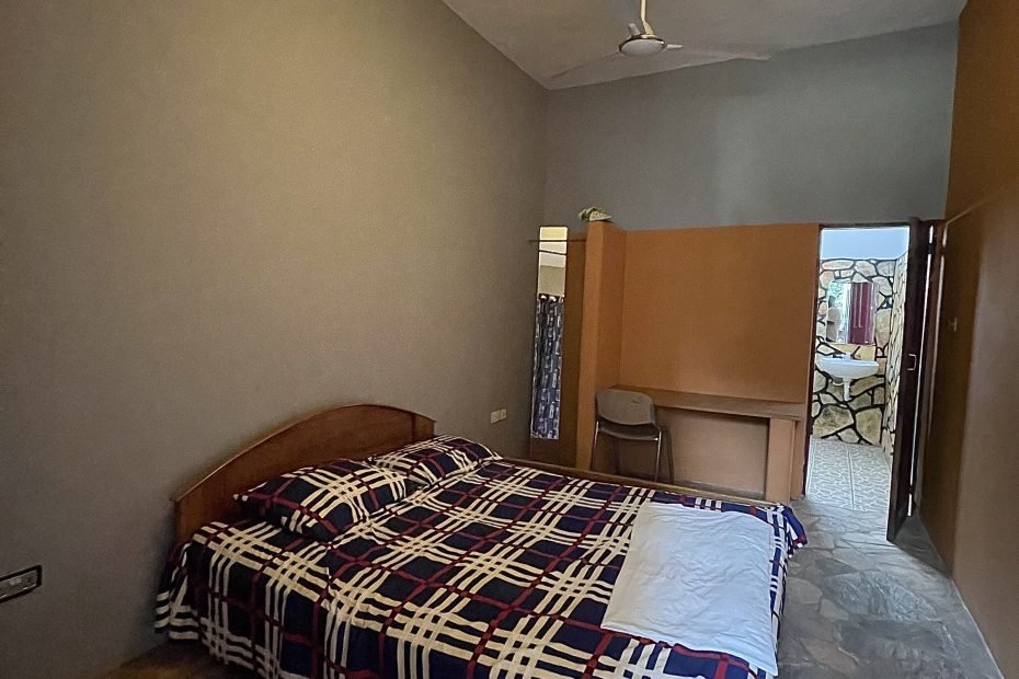 “Spacious hotel room with a large bed, elegant decor, and a stunning view of the Aburi hills through wide glass windows.”