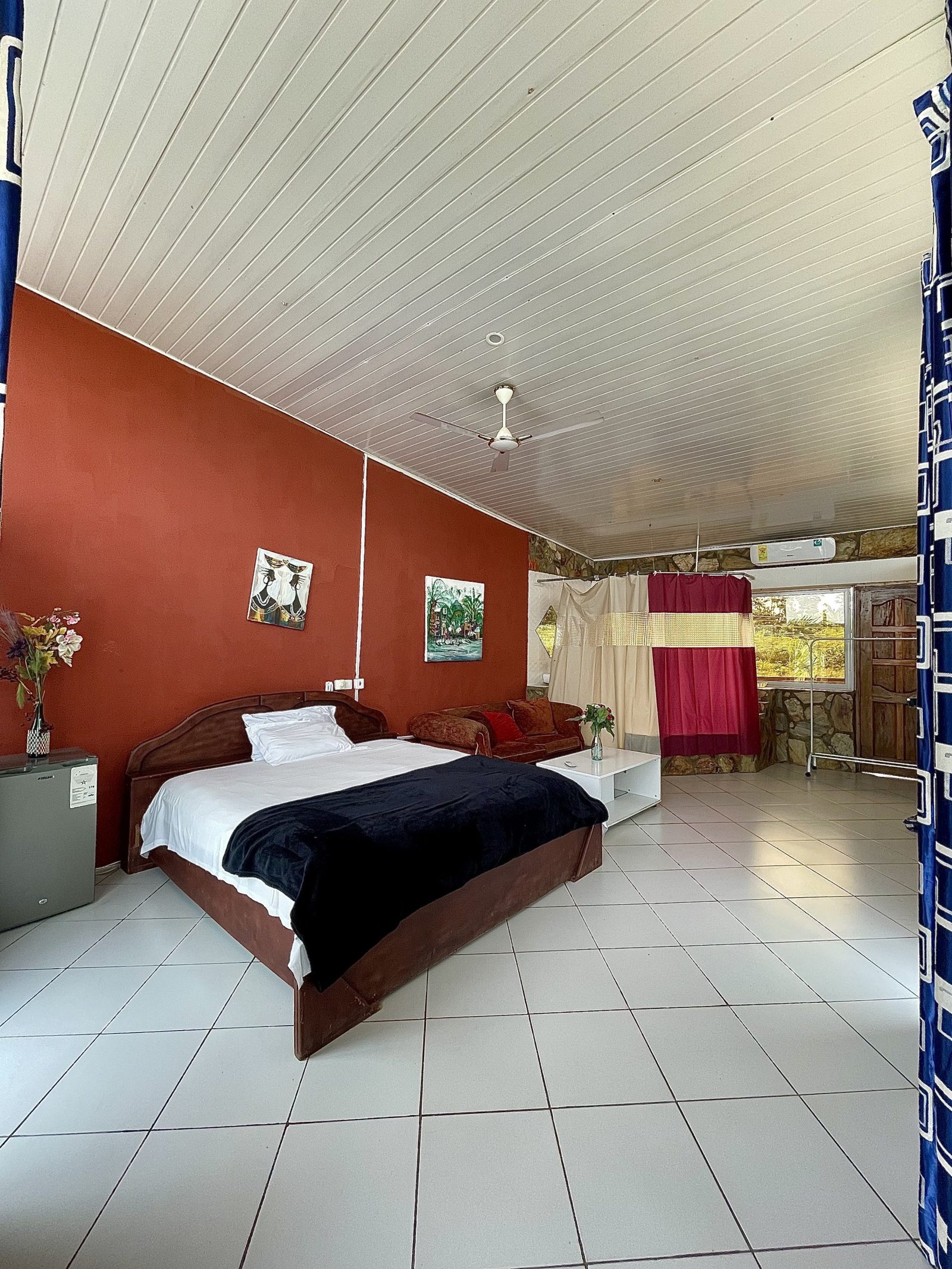 “Spacious hotel room with a large bed, elegant decor, and a stunning view of the Aburi hills through wide glass windows.”
