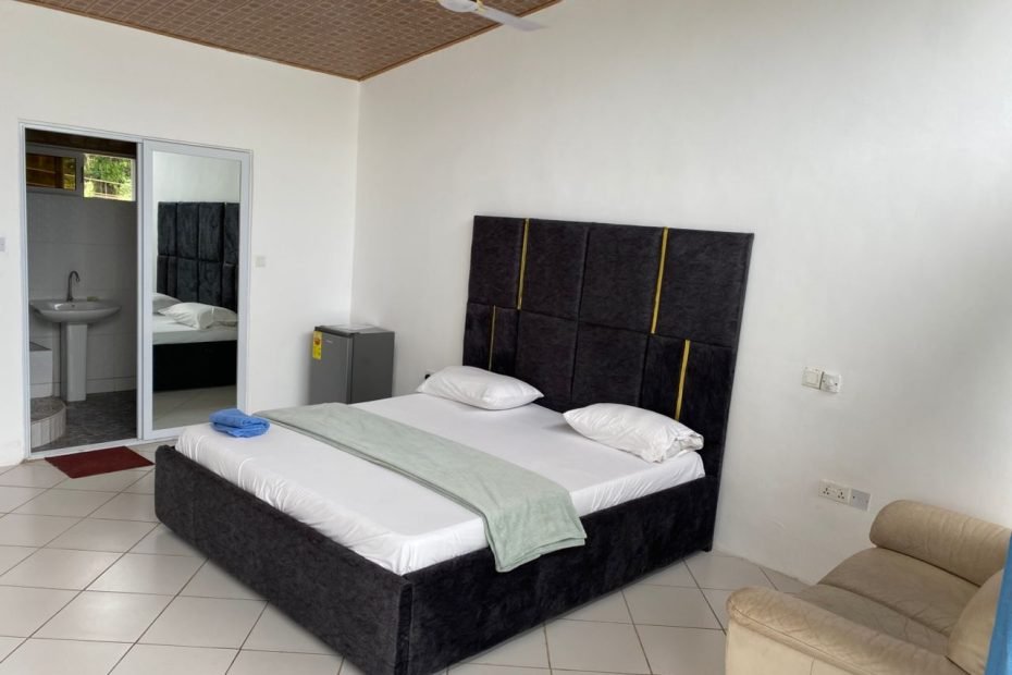“Spacious hotel room with a large bed, elegant decor, and a stunning view of the Aburi hills through wide glass windows.”